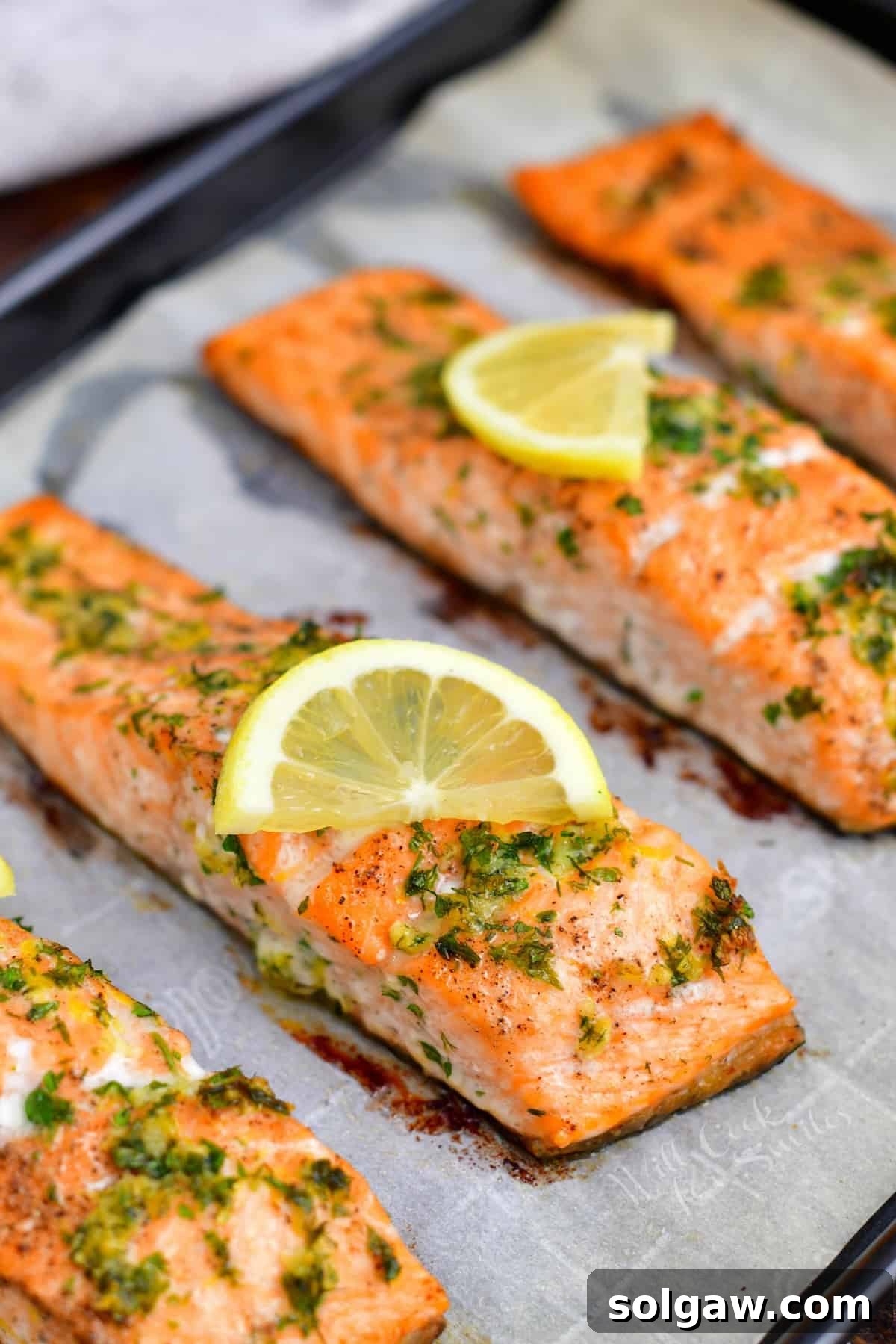 Closeup image of oven baked salmon fillets garnished with fresh herbs and bright lemon slices.