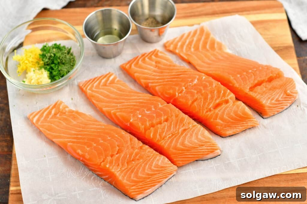Four fresh salmon fillets on parchment paper, ready to be seasoned with fresh herbs for a healthy salmon recipe.