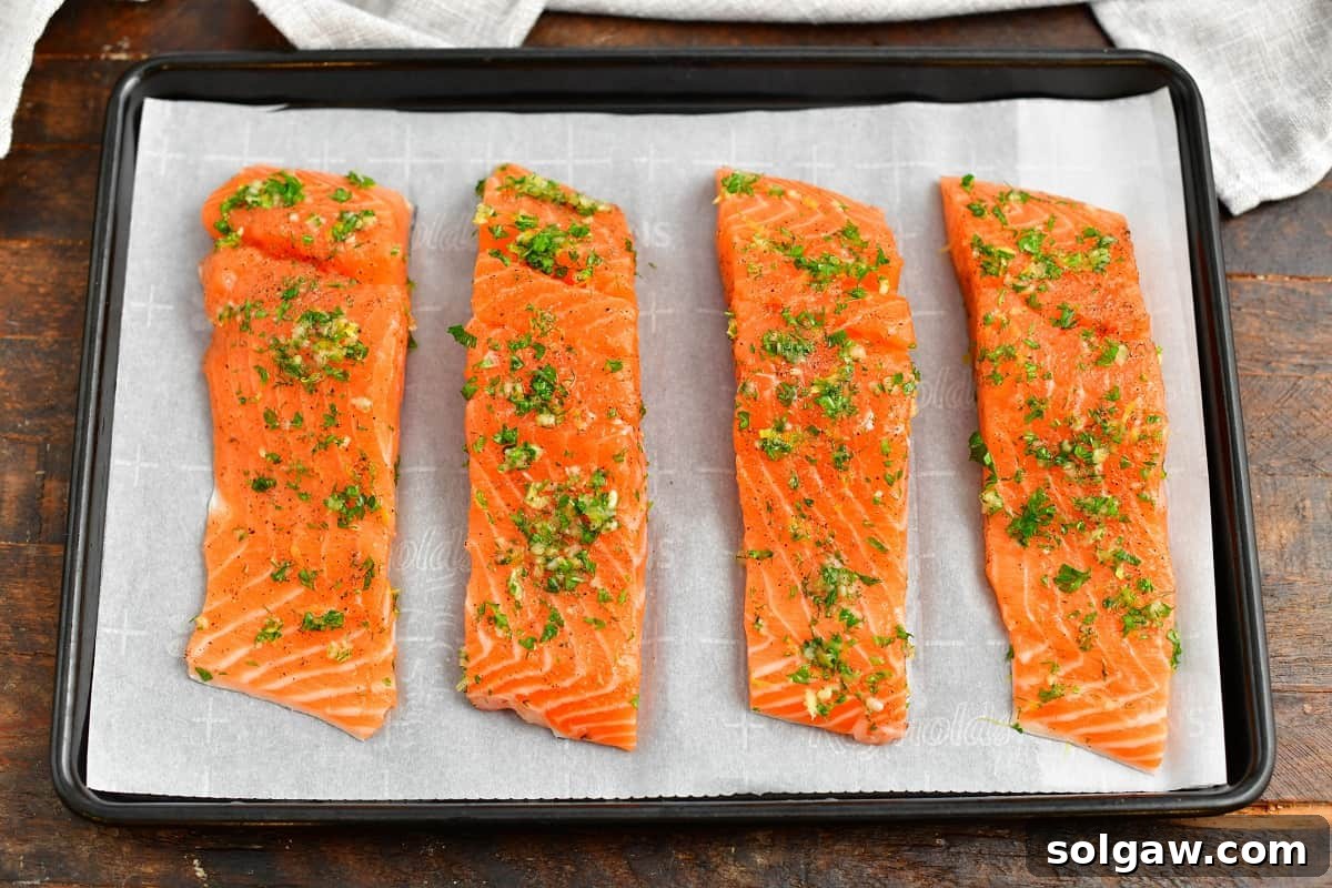 Four raw salmon fillets on a parchment-lined baking sheet, seasoned and ready for the oven.