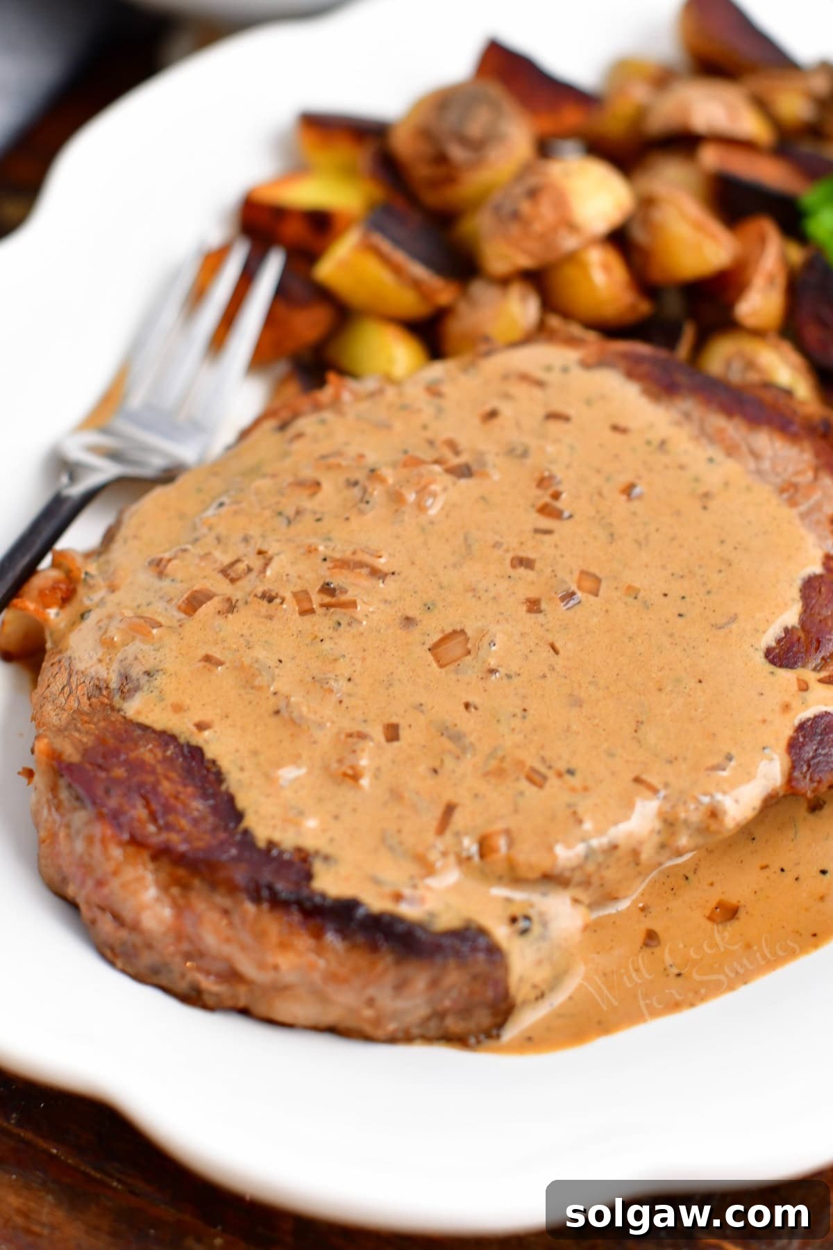 Juicy ribeye steak smothered in creamy peppercorn sauce, served with roasted potatoes, capturing a luxurious dining experience.