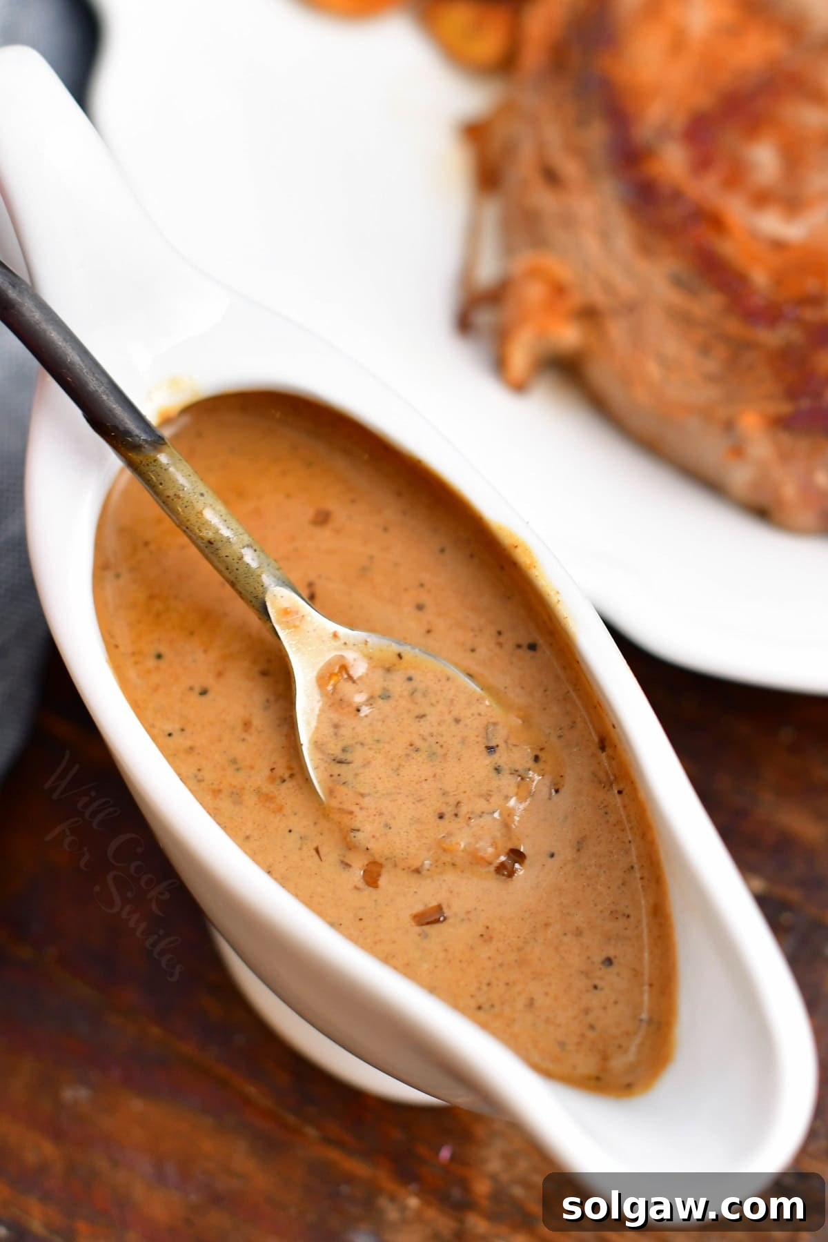 A creamy brown peppercorn sauce presented elegantly in a white gravy boat with a serving spoon, ready to be poured.