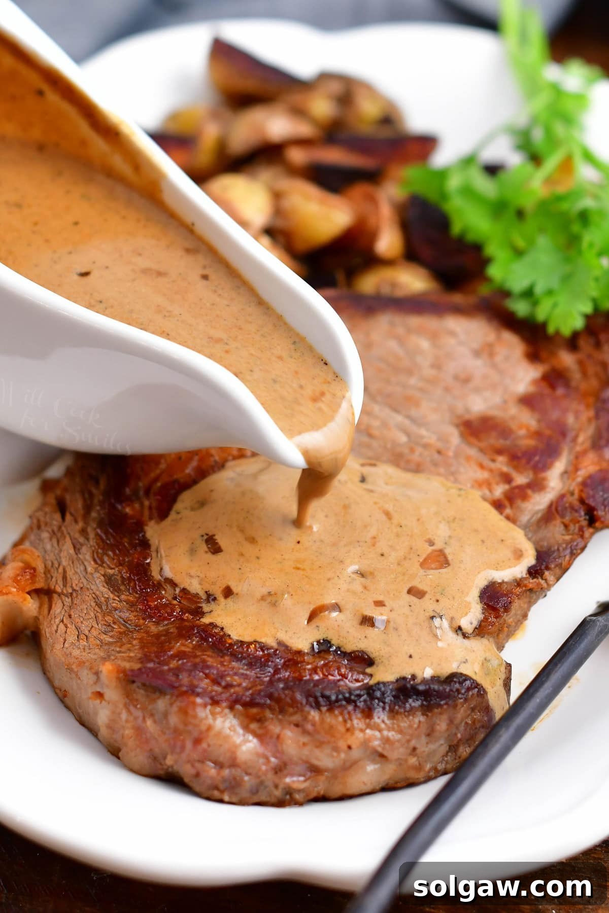 A generous pour of creamy peppercorn sauce cascading over a perfectly cooked steak on a pristine white platter, highlighting its rich texture.