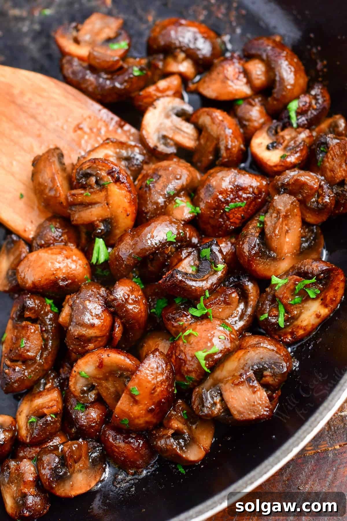 Finished bright sautéed mushroom halves in a skillet topped with fresh parsley