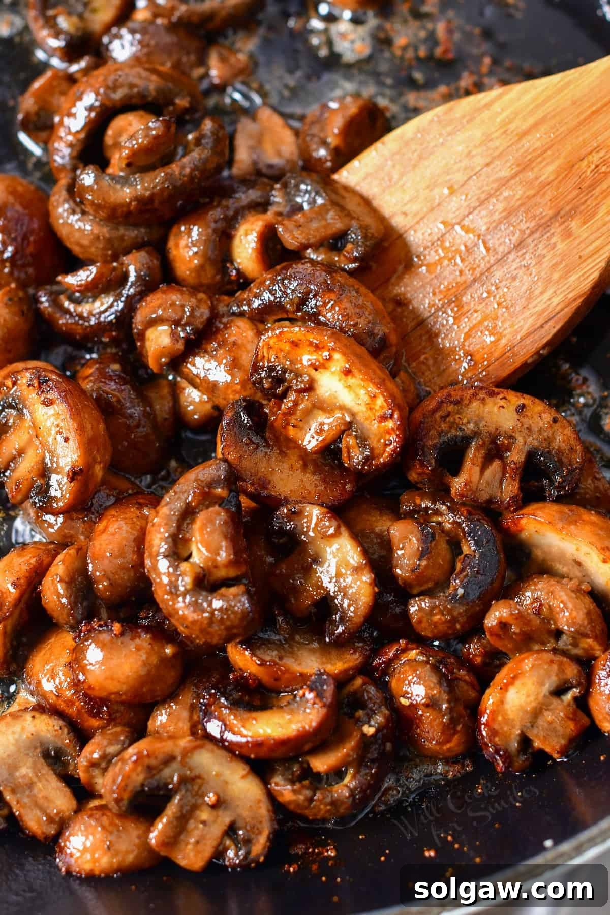 stirring sauteed mushrooms with wooden spoon in a skillet