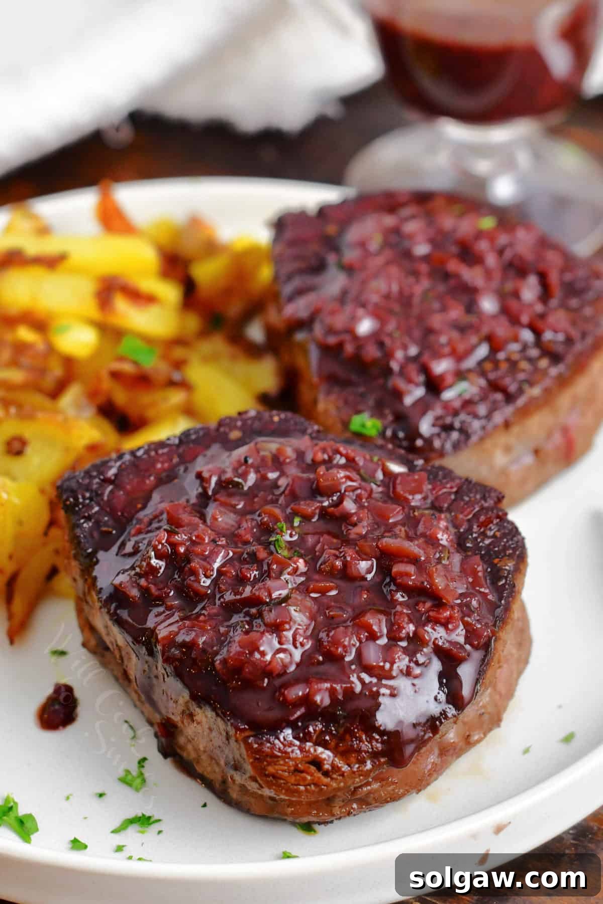 Perfectly seared steaks topped with luscious red wine steak sauce on a elegant plate, garnished with fresh herbs.