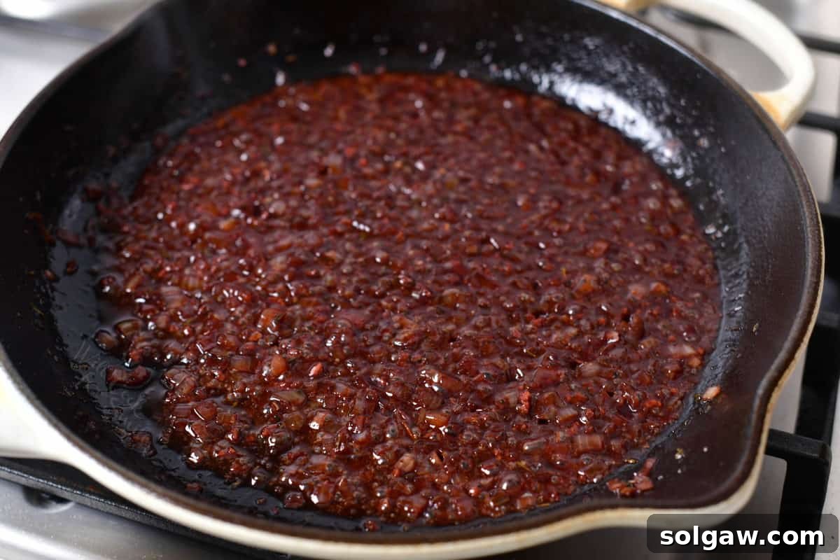 Shallots, garlic, and alcohol mixture simmering in a skillet until reduced, showing the depth of color developing.