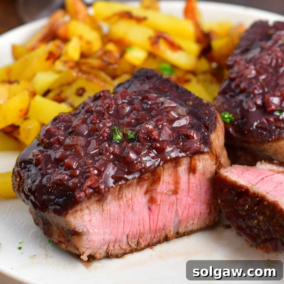 Closeup of a sliced tenderloin steak with luscious red wine sauce spooned over the top.