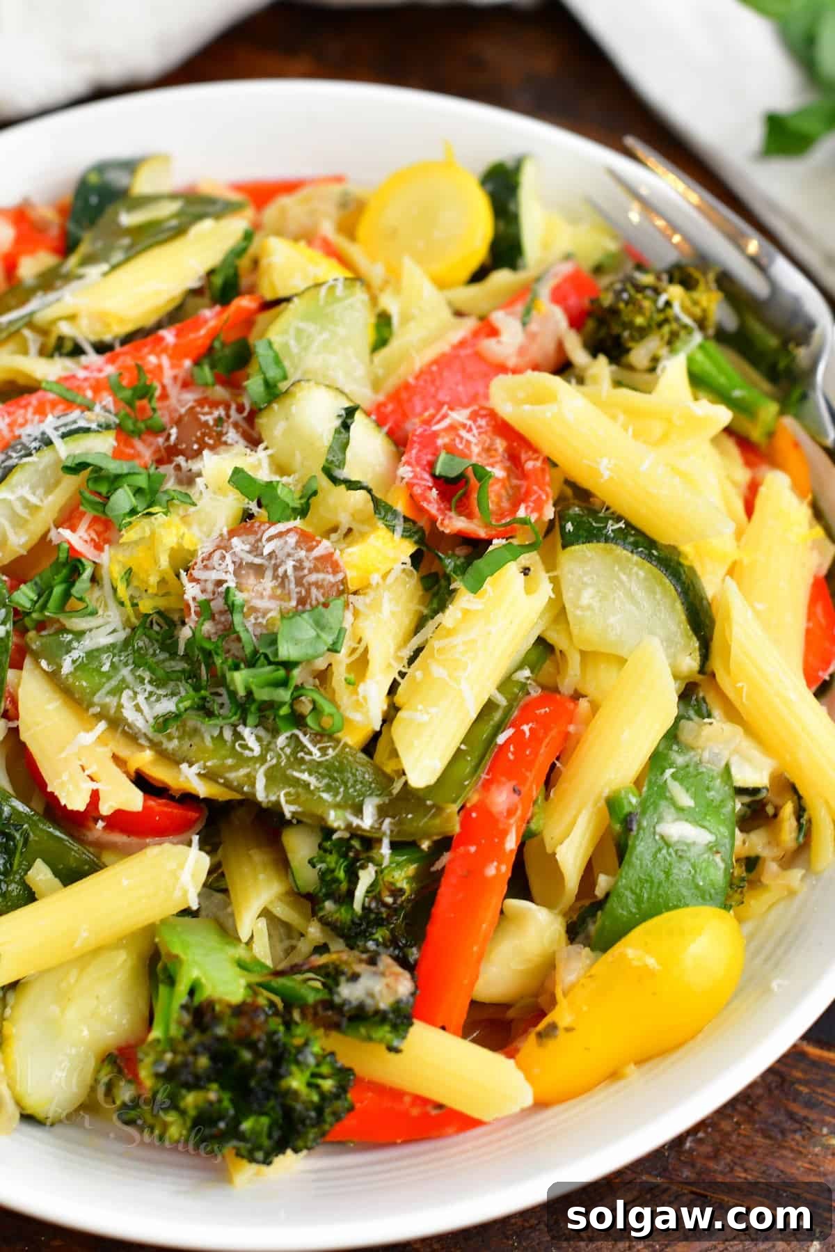 A large serving of colorful pasta primavera garnished with fresh basil on a white plate.