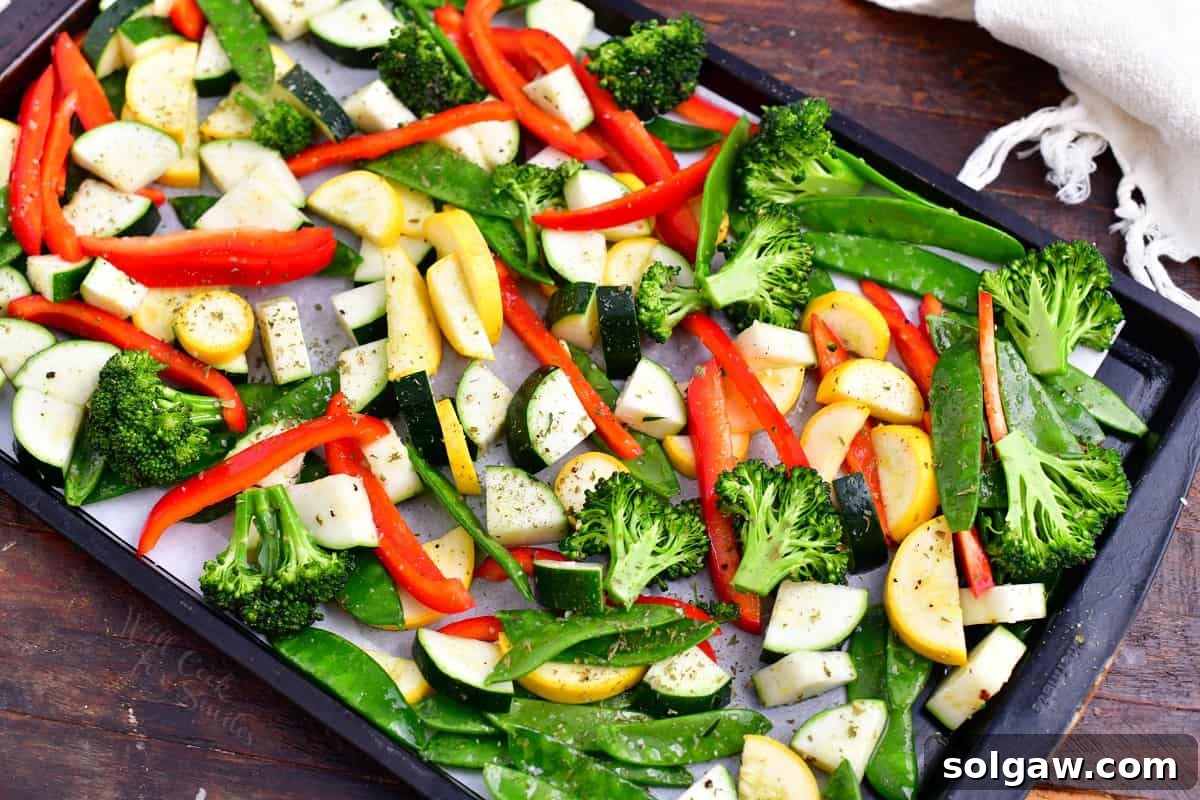 Chopped fresh vegetables seasoned with olive oil and herbs on a baking sheet, ready for roasting.