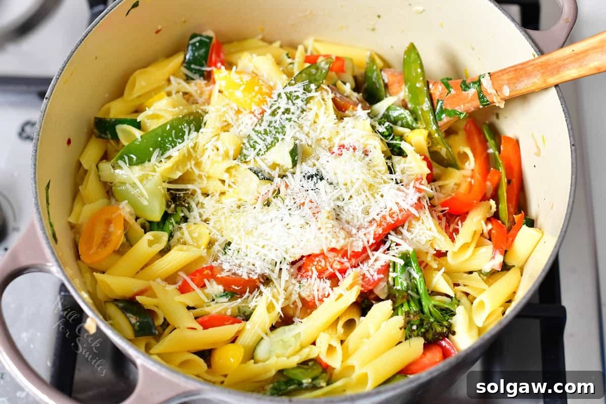 Fresh basil and lemon zest being stirred into the pasta primavera in a Dutch oven.