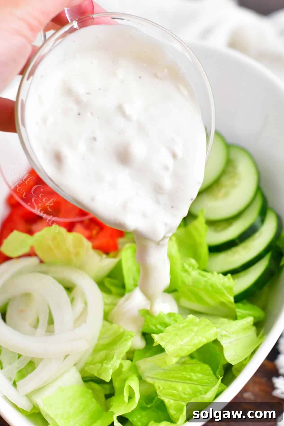 Blue cheese dressing is being poured on to a salad.