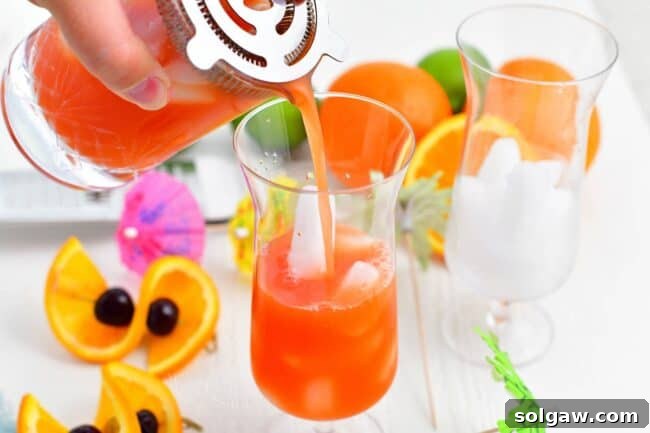 Tropical Rum Bliss 5 Vibrant rum punch is elegantly poured from a cocktail strainer into a glass filled with ice.