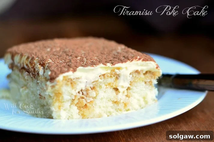 close up view 1 slice of tiramisu poke cake on decorative white dessert plate on wood table with fork in background to the right