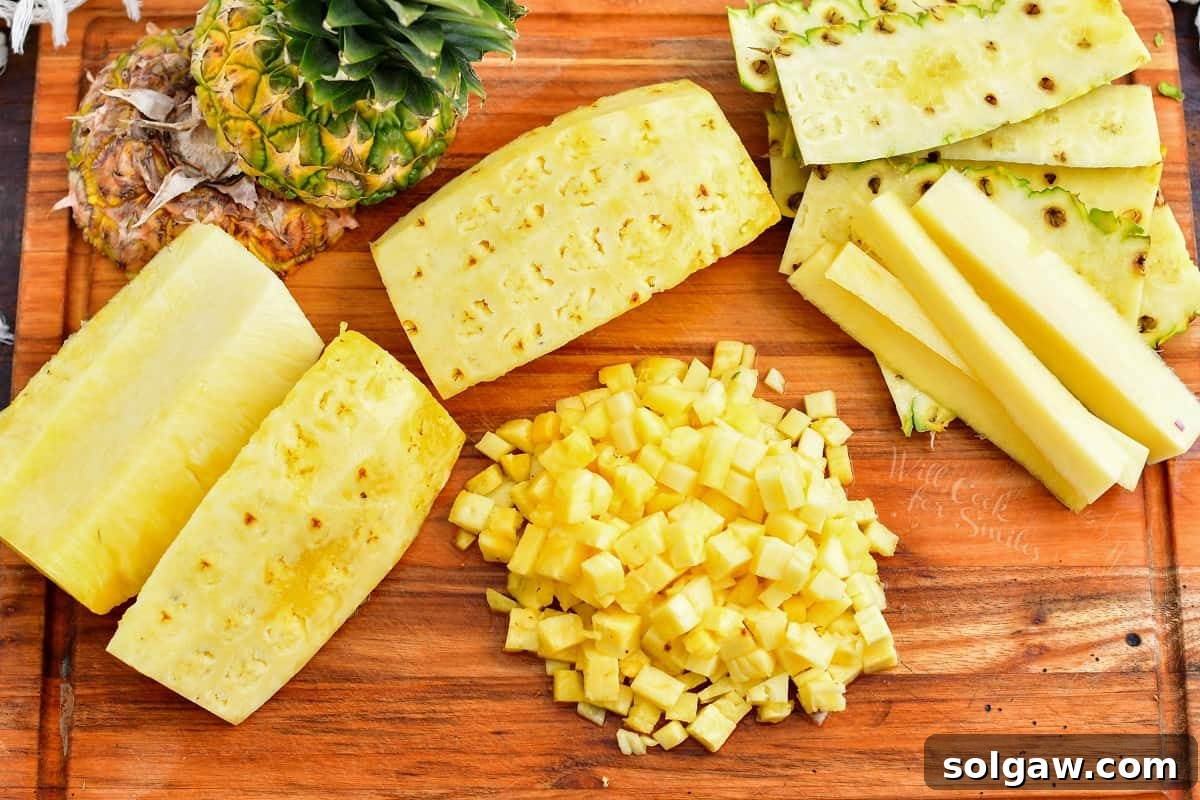 Various pineapple salsa ingredients, including a whole pineapple, bell pepper, red onion, jalapeños, and cilantro, are neatly arranged on a rustic wooden cutting board, ready for preparation.