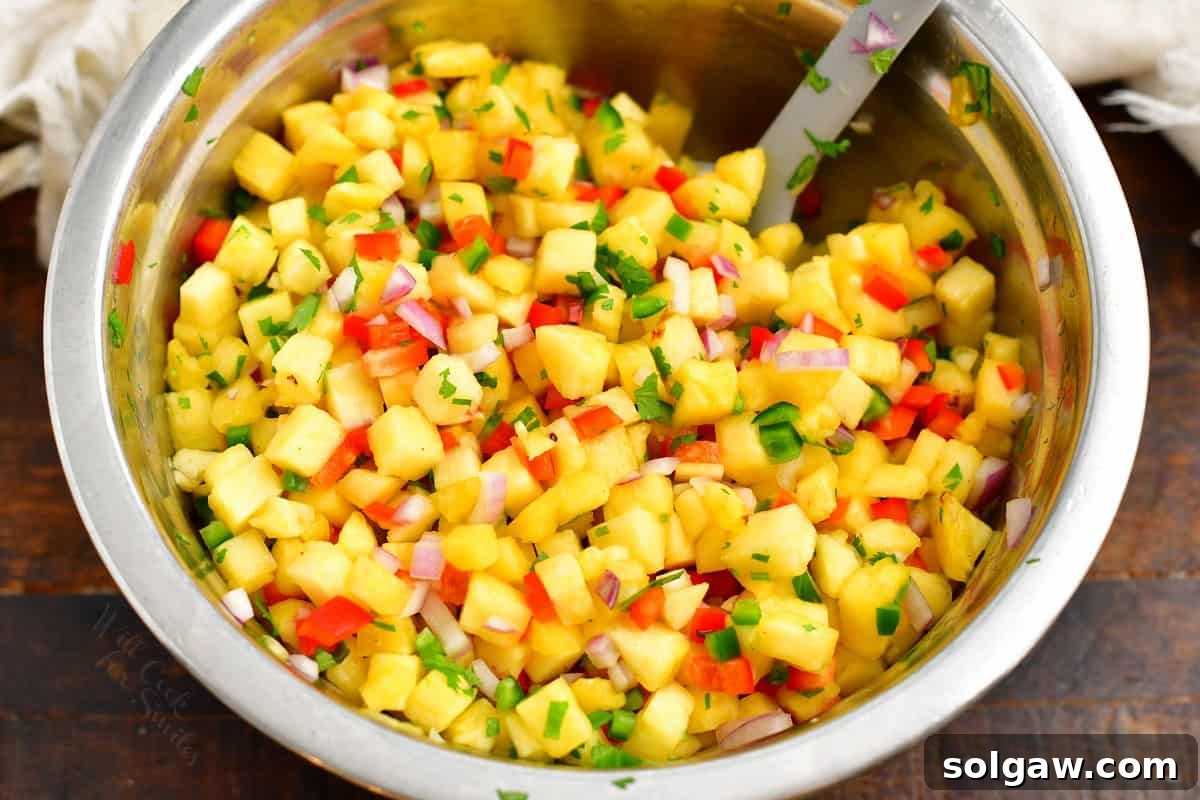 Freshly prepared pineapple salsa, a mix of diced pineapple, peppers, and cilantro, is thoroughly combined in a large, clear glass bowl, ready to be served.