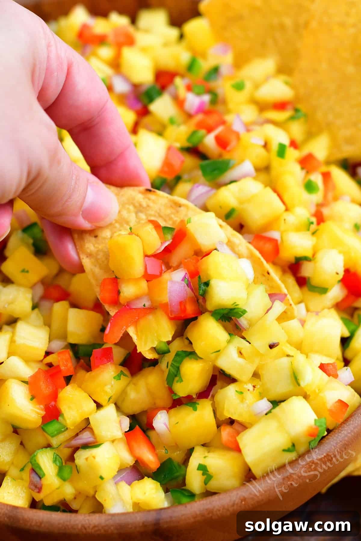A crispy tortilla chip scooping up a generous portion of colorful pineapple salsa, showcasing its texture and vibrant ingredients.