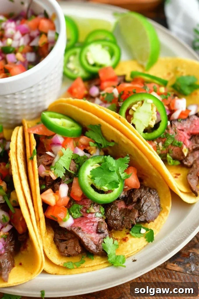 Festive Cinco De Mayo Food Ideas 2 Closer view of a perfectly grilled steak taco, garnished with vibrant pickled jalapeño rings, fresh pico de gallo, and a sprinkle of fragrant cilantro, served on a white plate.