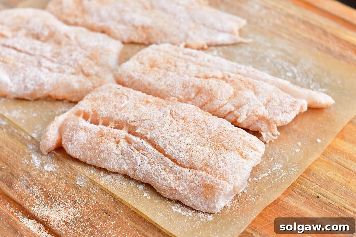 Uncooked cod is coated in flour and placed on a sheet of parchment paper. 