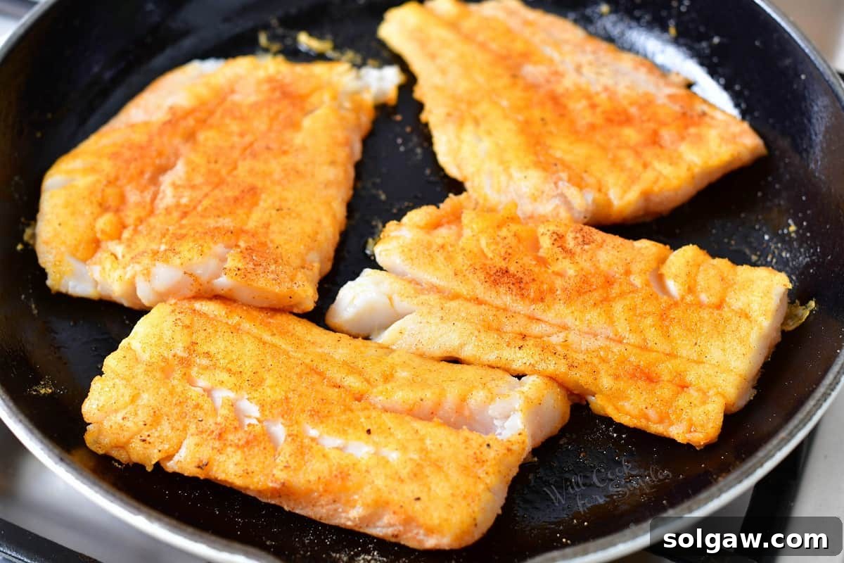 Cod is being seared in a large skillet.
