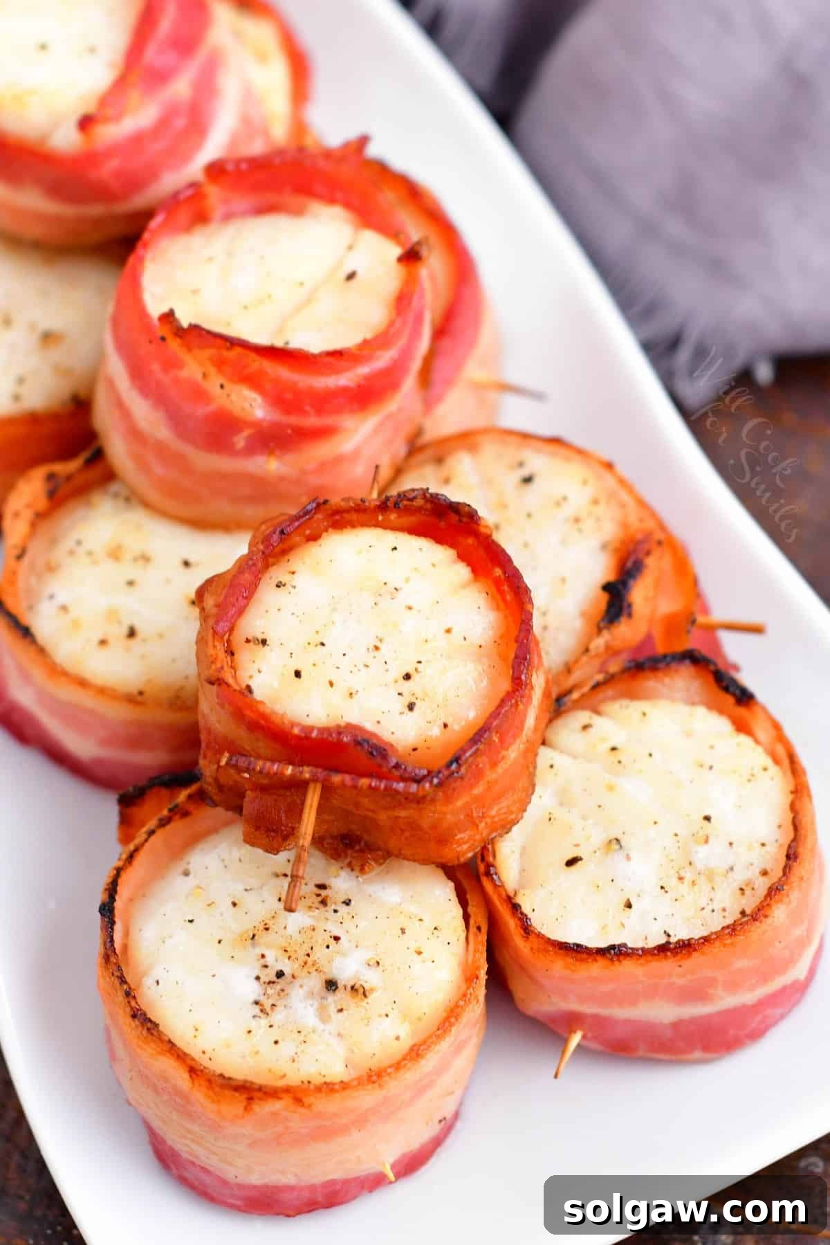 Scallops wrapped in bacon are piled on a rectangular white plate.