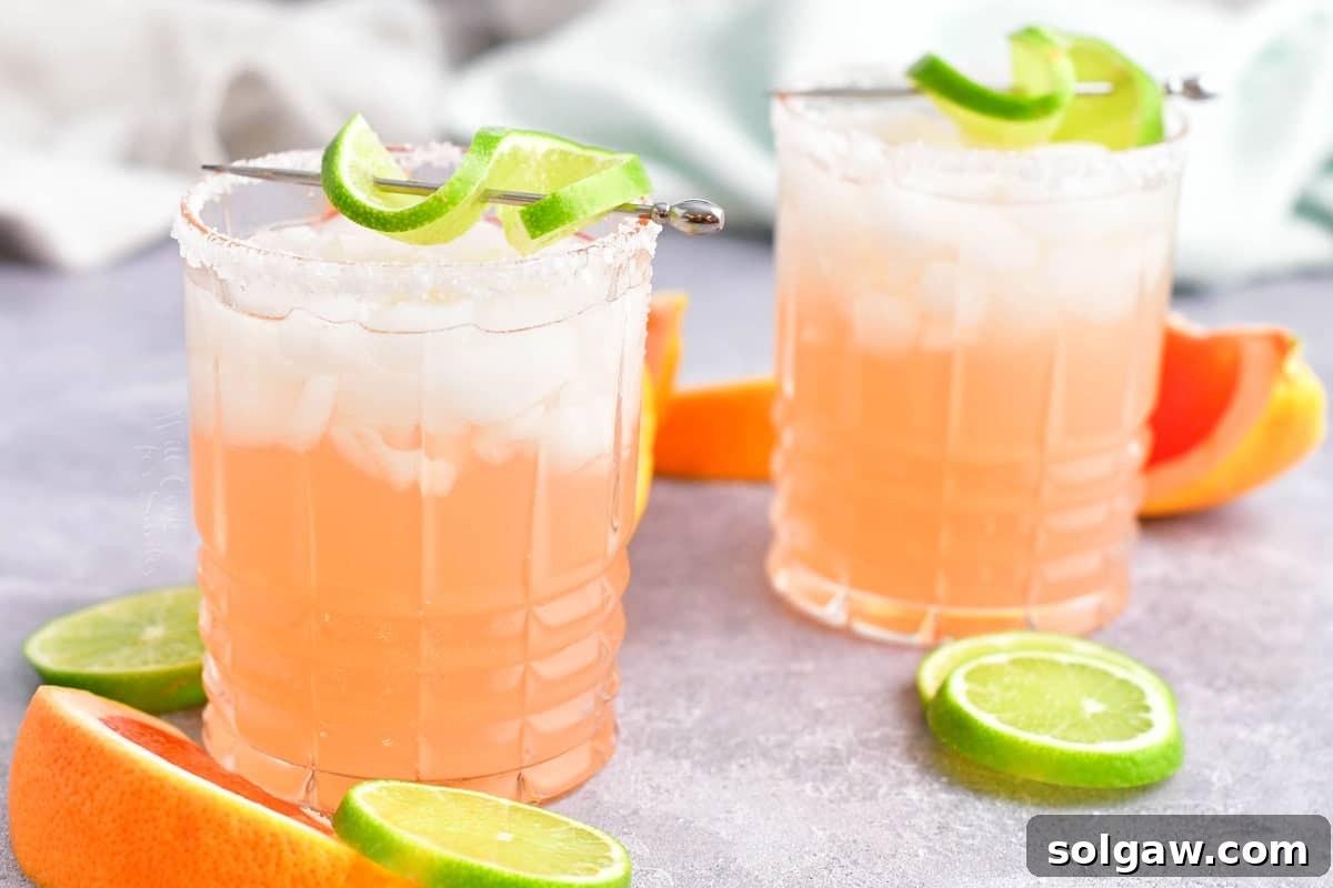 Two palomas, garnished with lime wedges, sit on a counter alongside fresh lime slices.