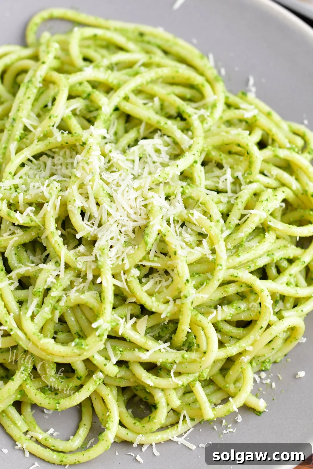 A vibrant plate of pesto pasta, generously sprinkled with freshly grated Parmesan cheese and a few basil leaves, ready to be enjoyed.