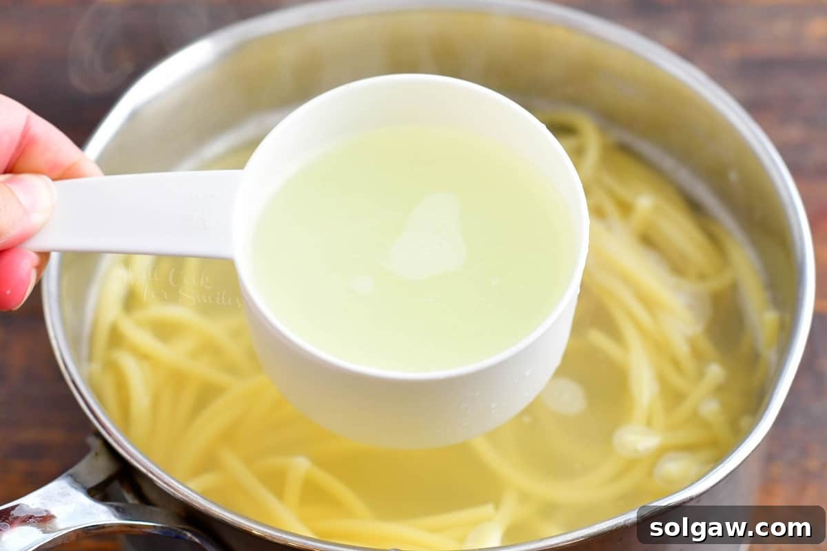 A measuring cup filled with starchy pasta water being carefully reserved from a pot of freshly boiled pasta, a crucial step for achieving a creamy and emulsified pesto sauce.