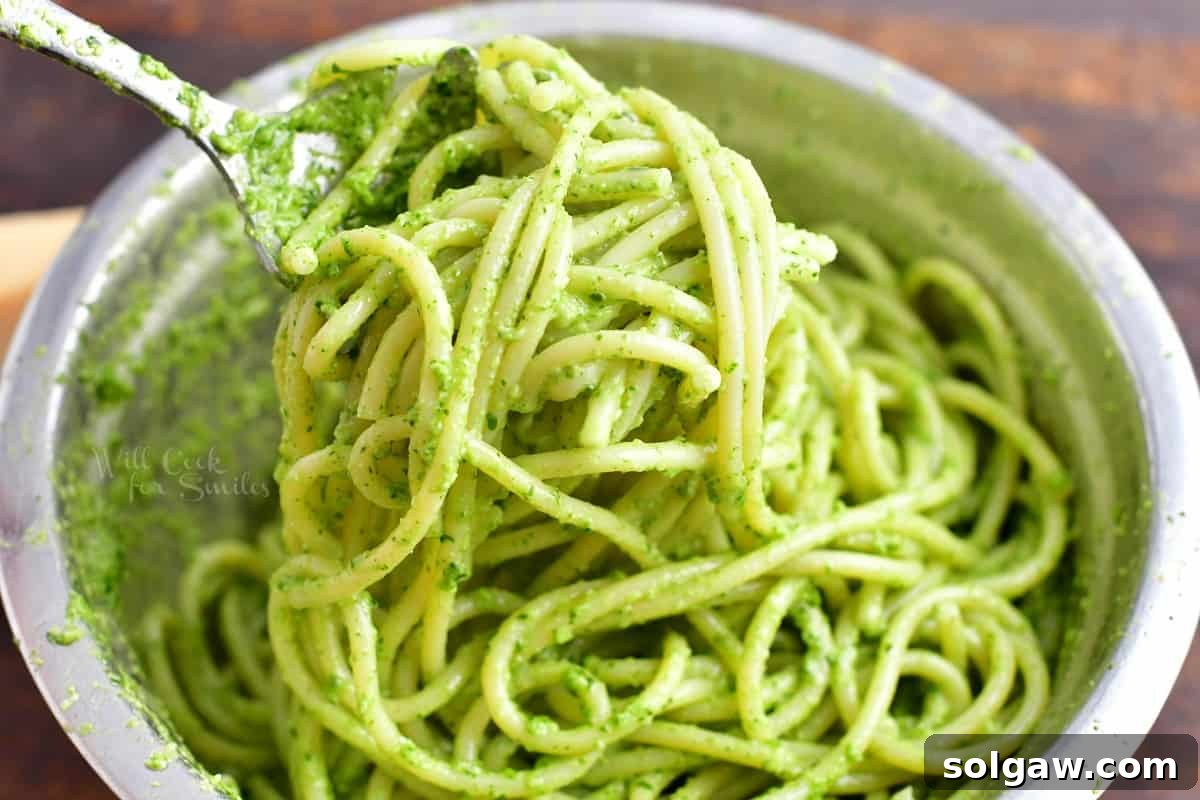 Delicious pasta being expertly tossed with rich pesto sauce and the essential starchy pasta water in a large white bowl, ensuring every piece is perfectly coated for a creamy finish.