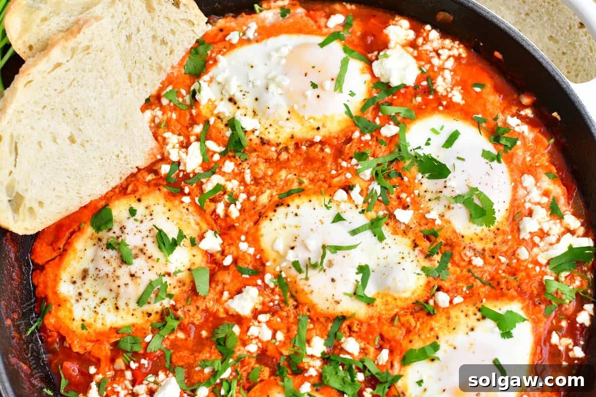 Close-up shot of a perfectly cooked Shakshuka in a black skillet, garnished with fresh green herbs, highlighting the well-set egg whites and runny yolks amidst the rich tomato sauce.