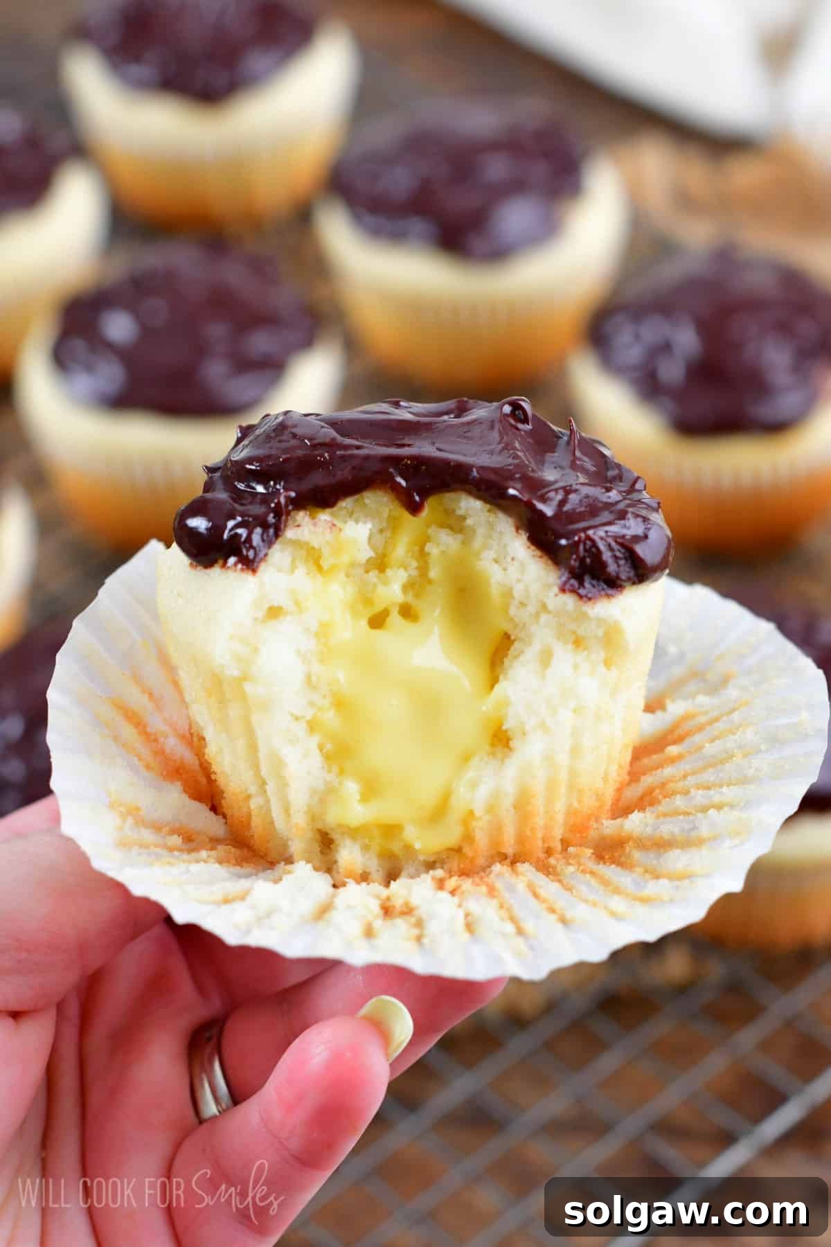 Holding a Boston cream cupcake with a bite taken out of it.
