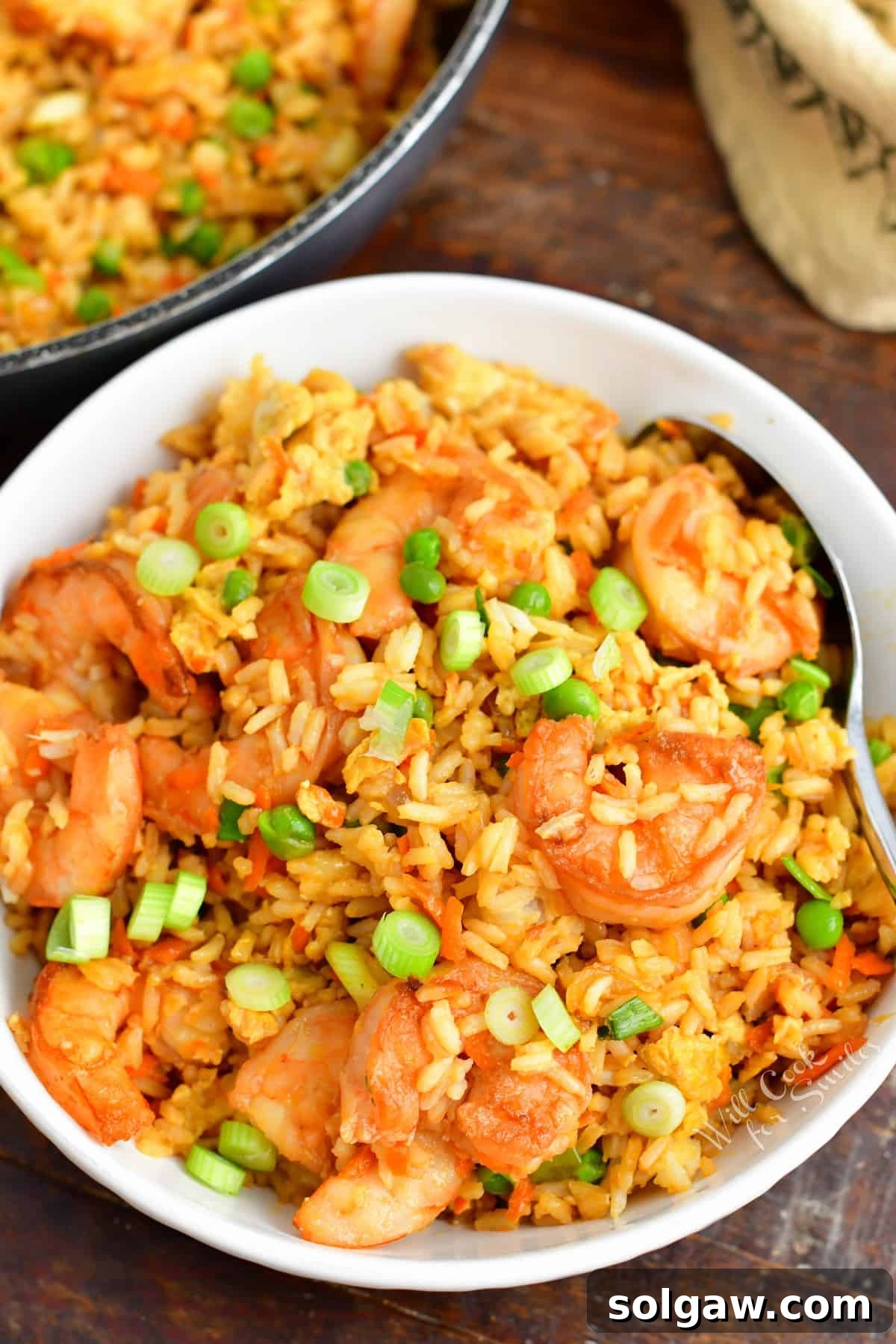 Shrimp fried rice is in a white bowl with a spoon.
