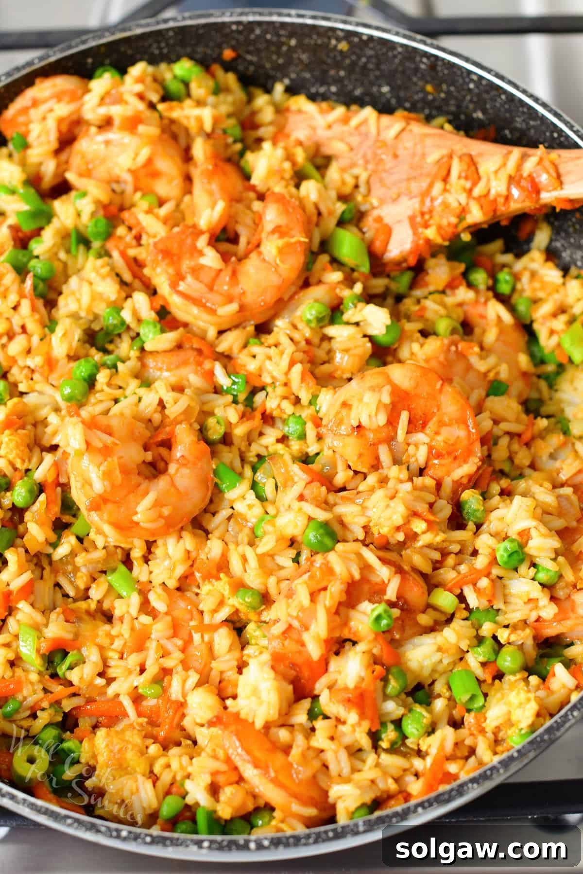 A wooden spoon is placed in a pan filled with shrimp fried rice.