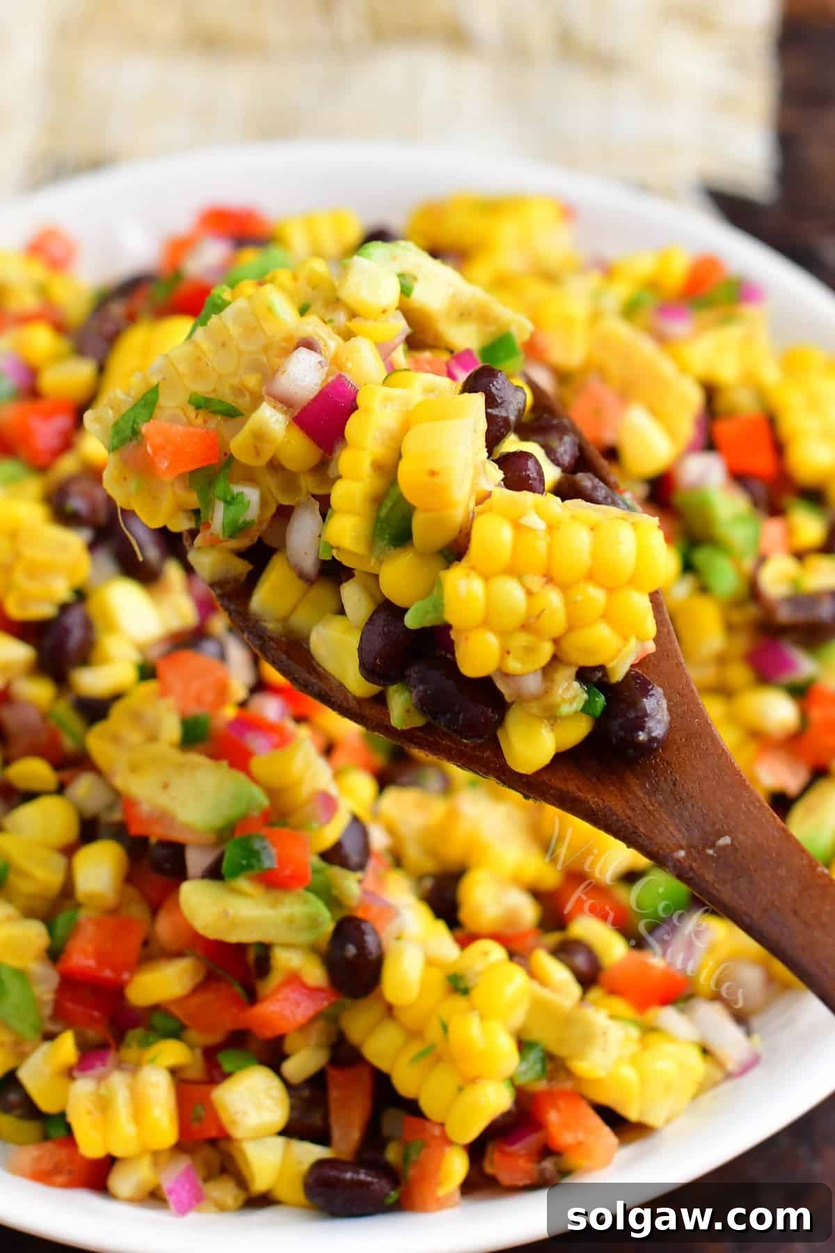 A wooden spoon is scooping a serving of salad from a large white bowl. 