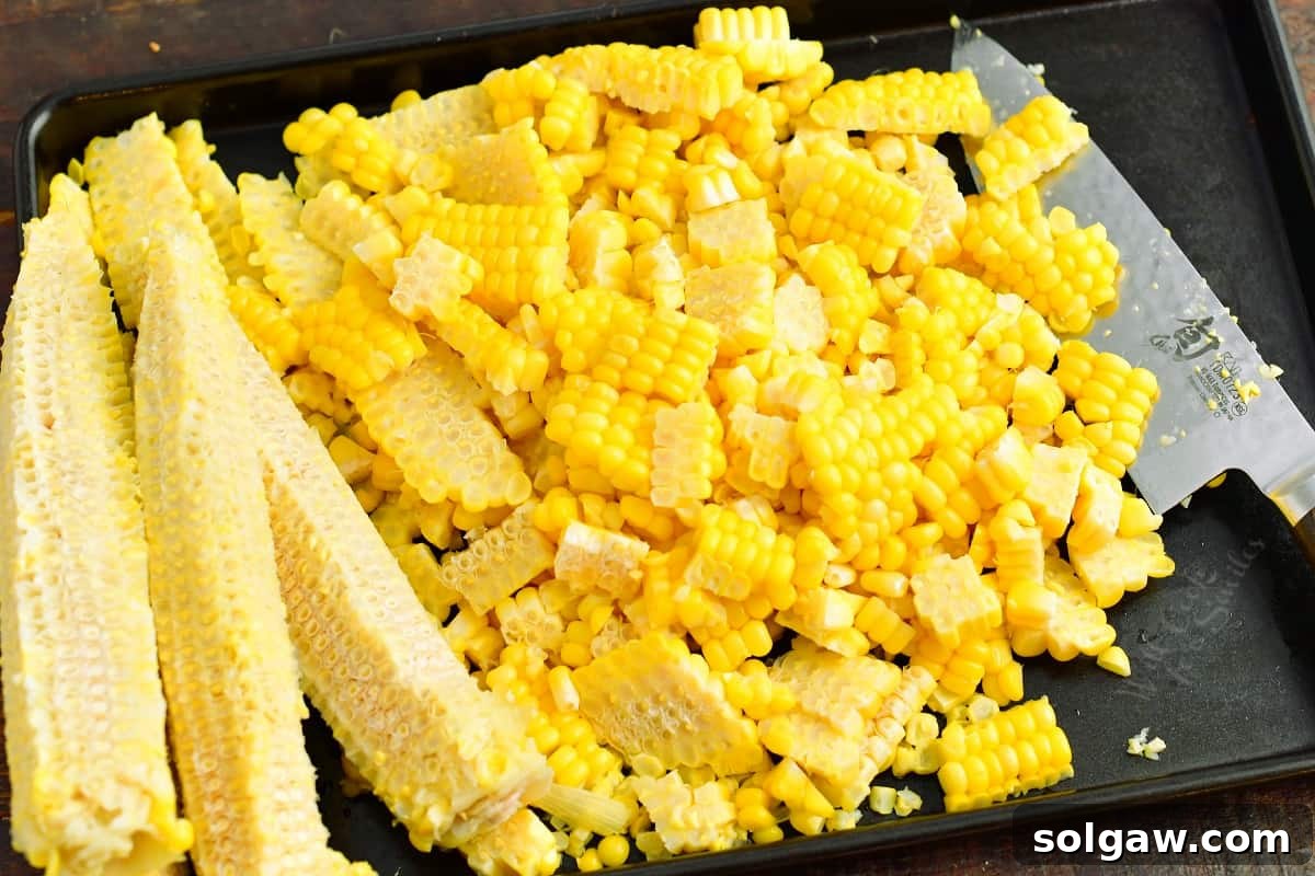Corn kernels that were cut off of the cob on a baking sheet with a knife next to them. 