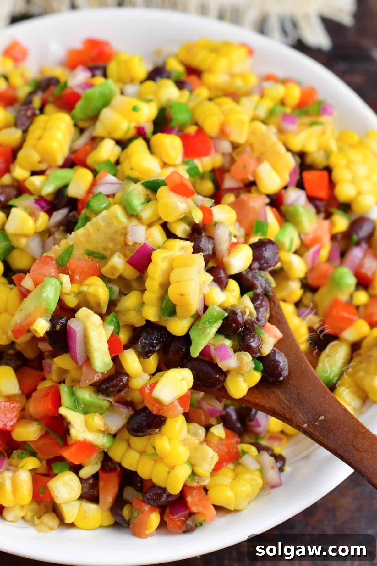 The salad is being lifted from the bowl with a wooden spoon. 