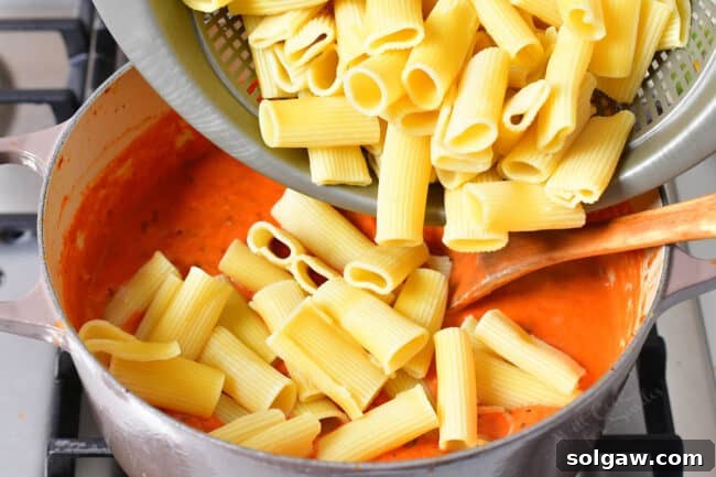 Creamy Tomato Vodka Penne 7 Cooked noodles are being poured into the pot full of sauce.