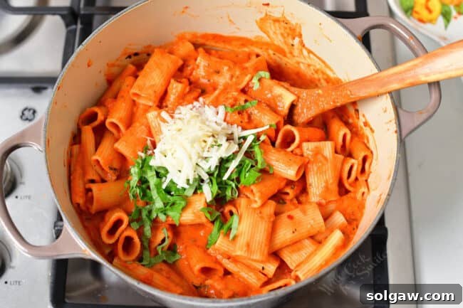 Creamy Tomato Vodka Penne 8 A pot is filled with basil and parmesan on top of coated noodles.