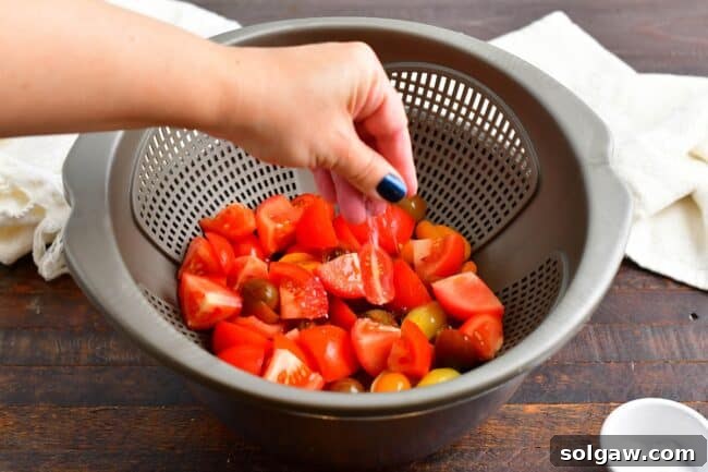 Sliced tomatoes in a colander, sprinkled with salt, ready to release their juices.