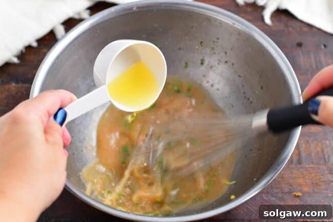Olive oil being slowly drizzled into a bowl of vinaigrette ingredients while whisking.