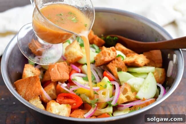 Tomato vinaigrette being poured over the salad ingredients in a bowl.