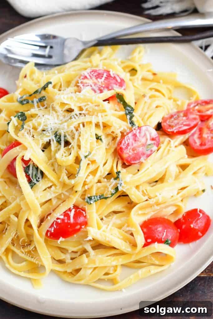Top view of creamy fettuccine on a plate with fresh tomatoes, basil, and a sprinkle of Parmesan cheese, ready to be enjoyed.