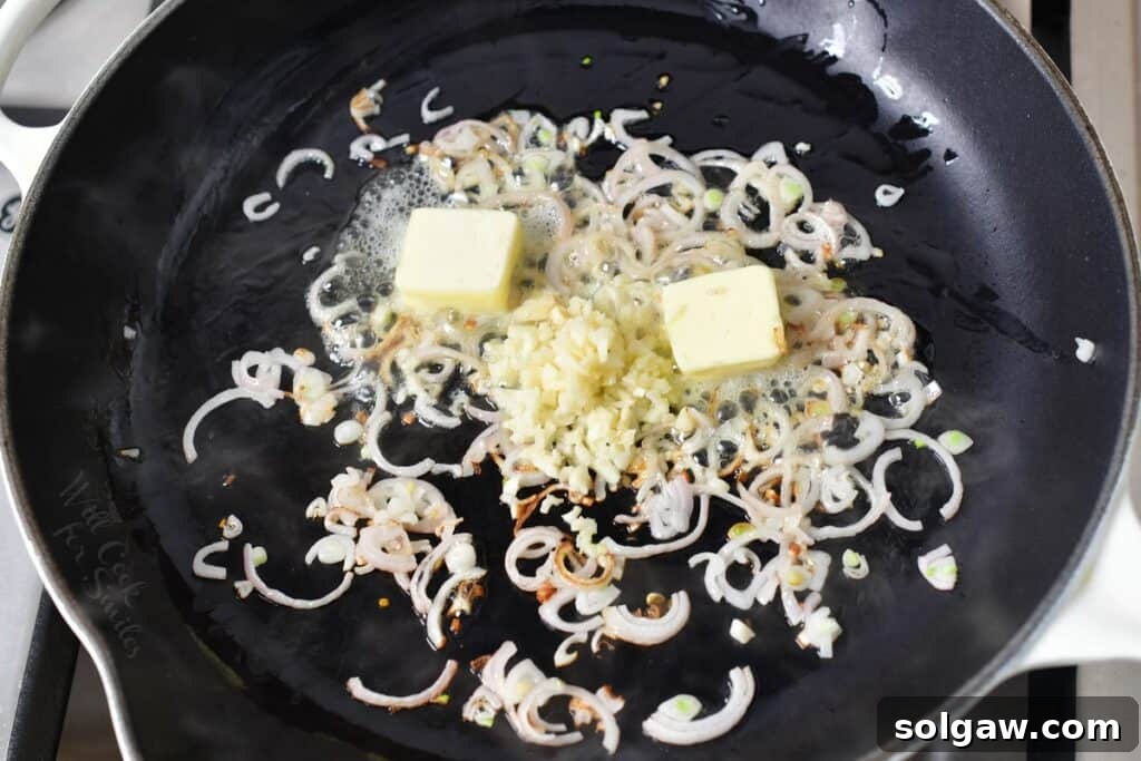 Butter, minced garlic, and sliced shallots sautéing together in a hot cooking pan, forming the aromatic base of the cream sauce.