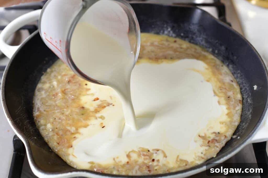 Adding rich heavy cream to the simmering shallot and garlic mixture in a pan, beginning the transformation into a luscious cream sauce.