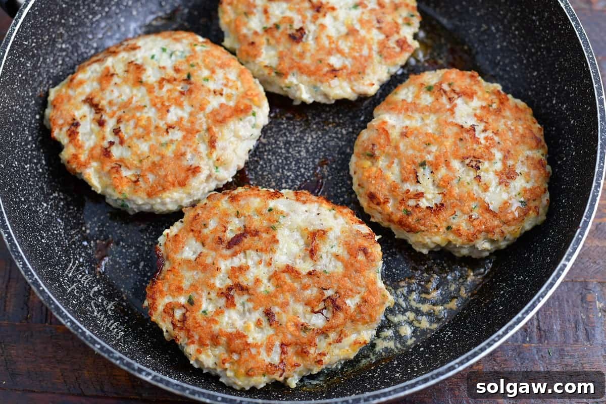 Ultimate Chicken Burgers 6 Four golden-brown cooked chicken burger patties in a large pan, demonstrating the perfect sear.