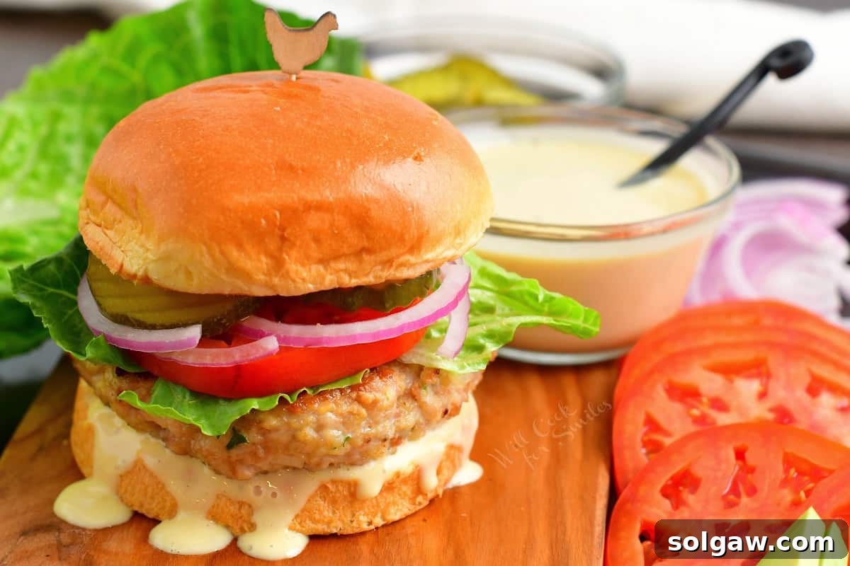 Ultimate Chicken Burgers 9 A fully assembled chicken burger on a brioche bun with fresh lettuce, tomato, onion, and creamy sauce, ready to be enjoyed.