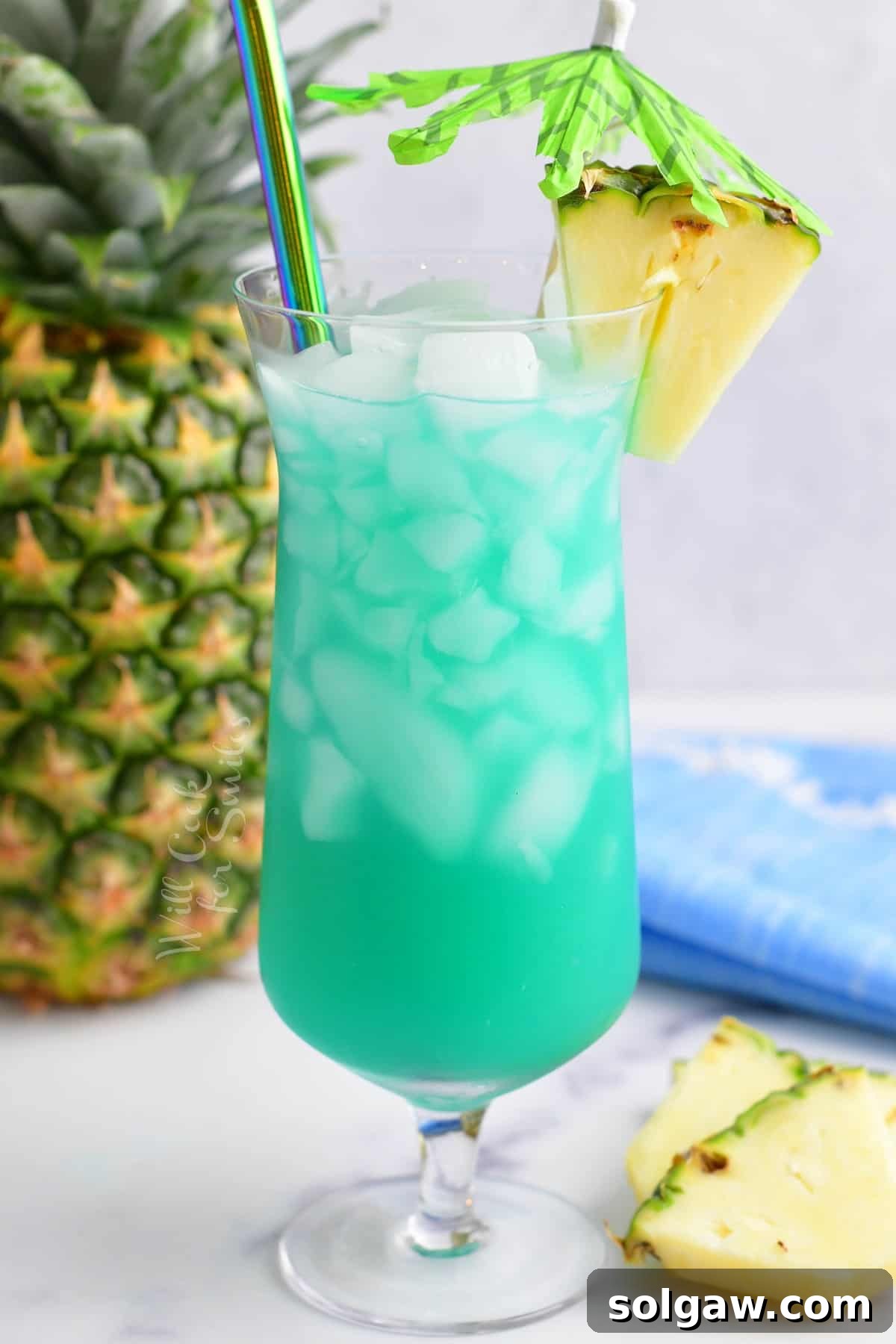 A tall hurricane glass overflowing with a bright blue Blue Hawaii cocktail, garnished with a pineapple slice and a red cherry, perfectly chilled and inviting.