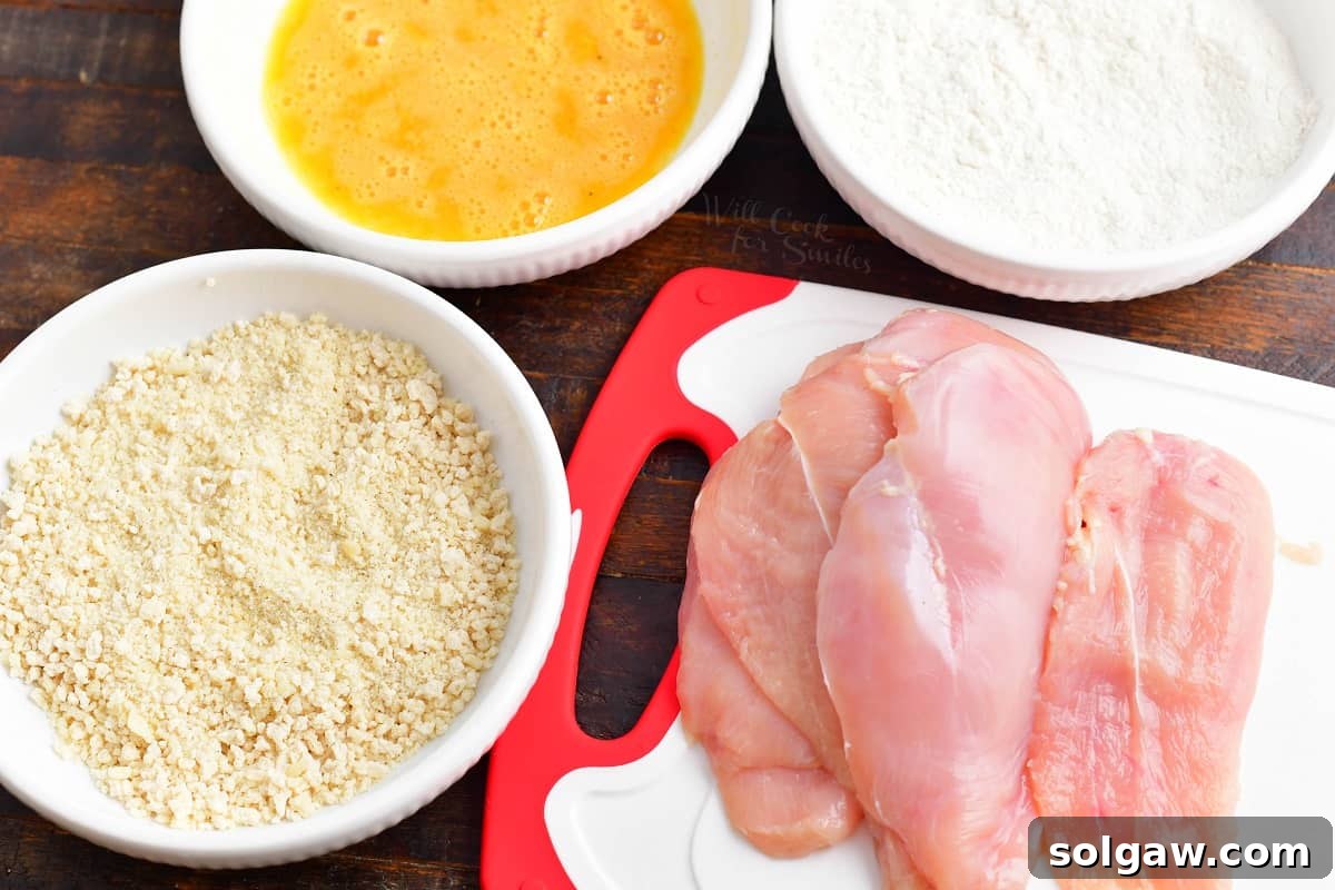 The ingredients for chicken milanese are plated on a wooden surface. 
