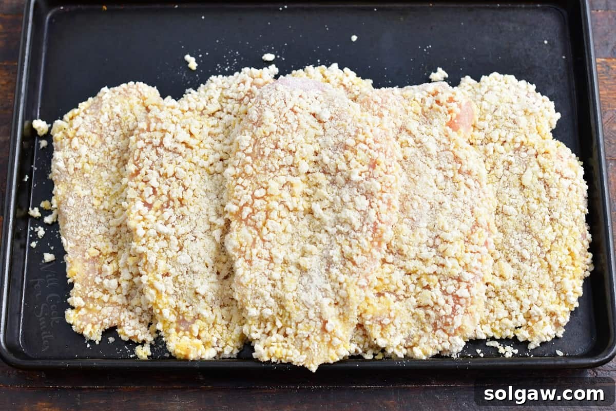 Several panko coated chicken breasts are on a black surface. 