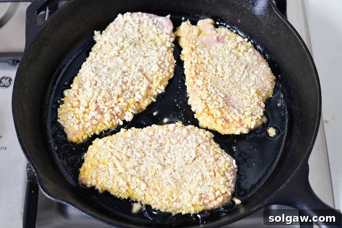 Three chicken breasts are being cooked in a black pan. 