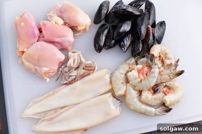 A Family's Cherished Paella 4 Various cuts of raw meat and seafood, including chicken thighs, calamari rings, and shrimp, are arranged on a white cutting board, ready for paella preparation.